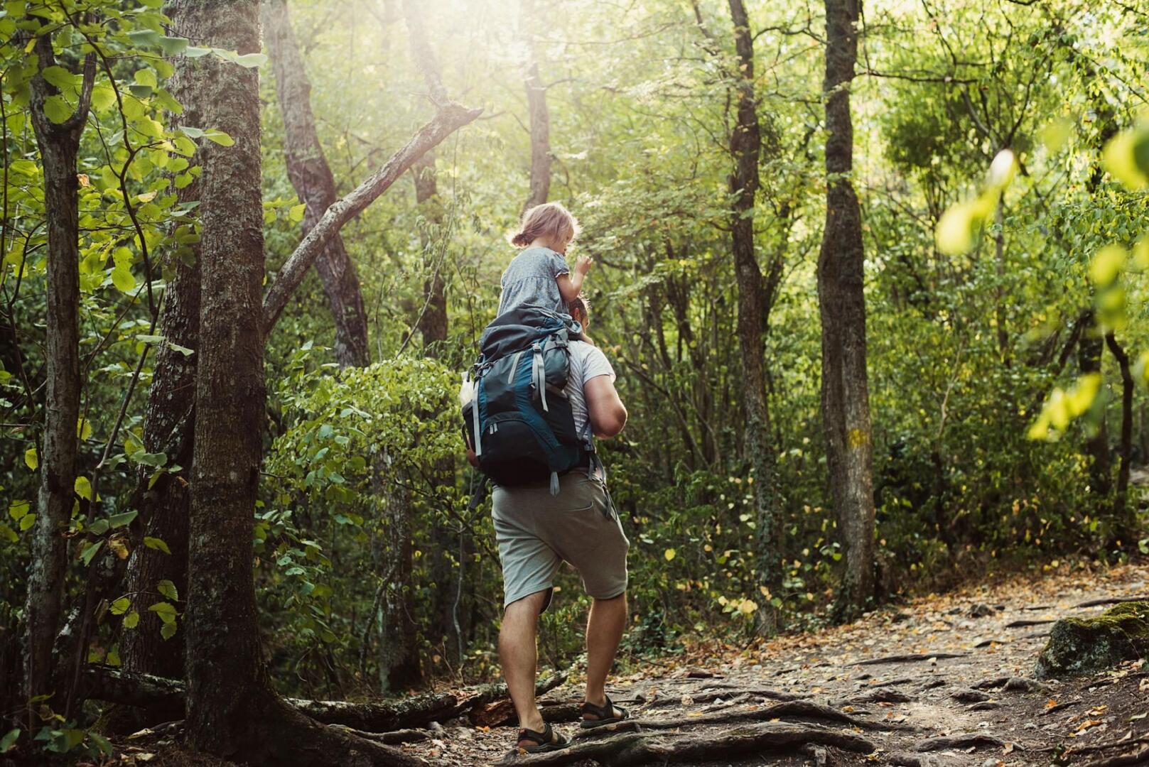 Mädchen von hintern, das auf den Schultern eines Mannes durch den Wald getragen wird.